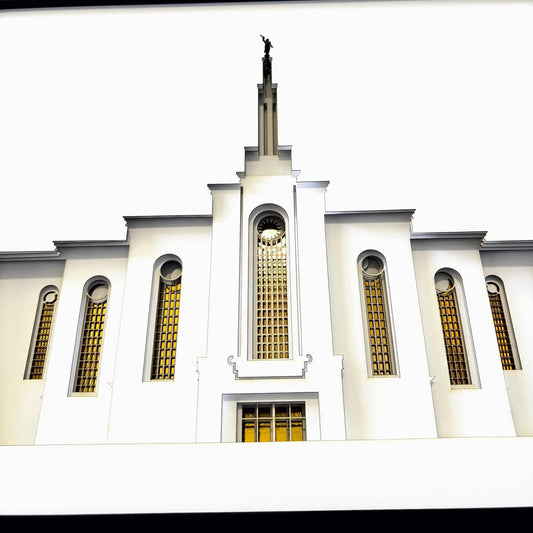 Front-facing view of a white temple building with tall arched windows featuring yellow-tinted glass and a central spire topped with a statue, shown against a bright sky.