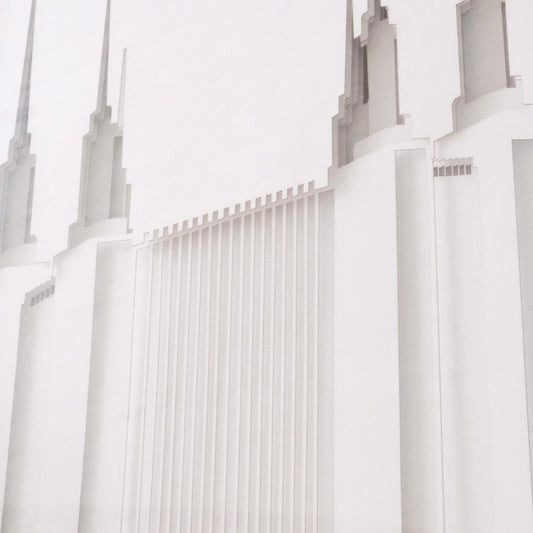 A close-up architectural photograph of a white temple-like building with tall spires and vertical ribbed detailing, shown against a very light neutral background.