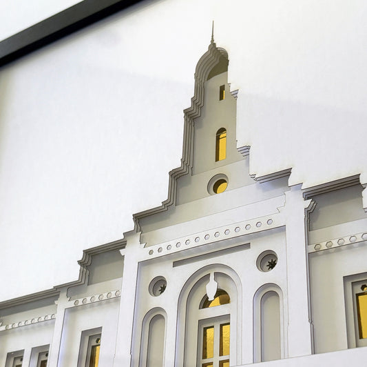 A close-up of a white architectural model or miniature building facade with gray trim, arched windows, and small gold-toned window accents, photographed against a white background.