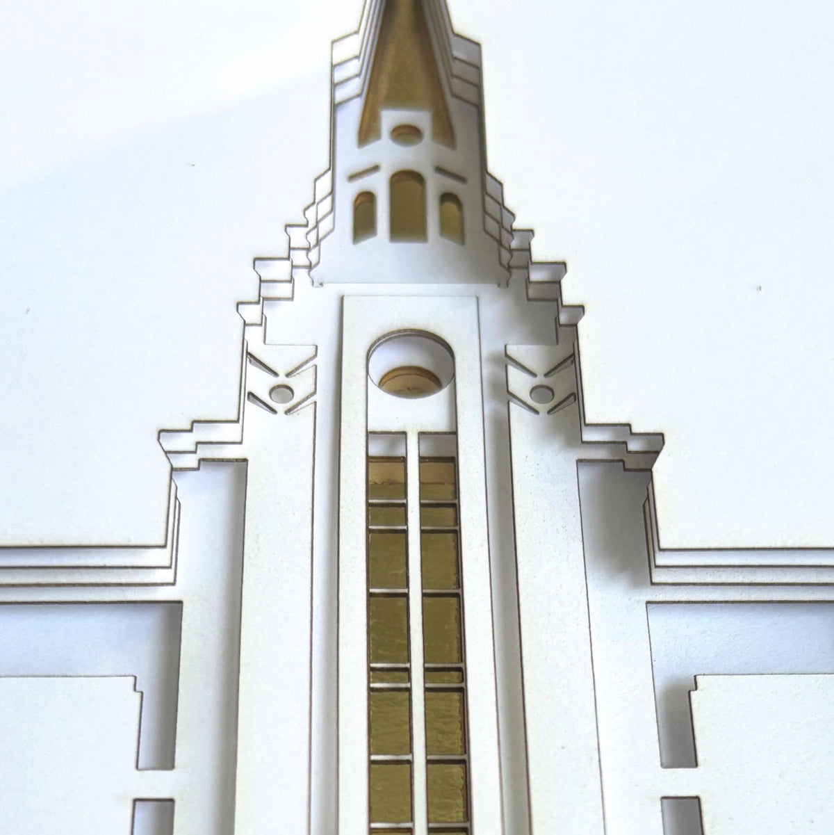 A close-up of a white laser-cut paper temple art architectural model or decorative sculpture featuring a pointed spire and geometric Art Deco style details.