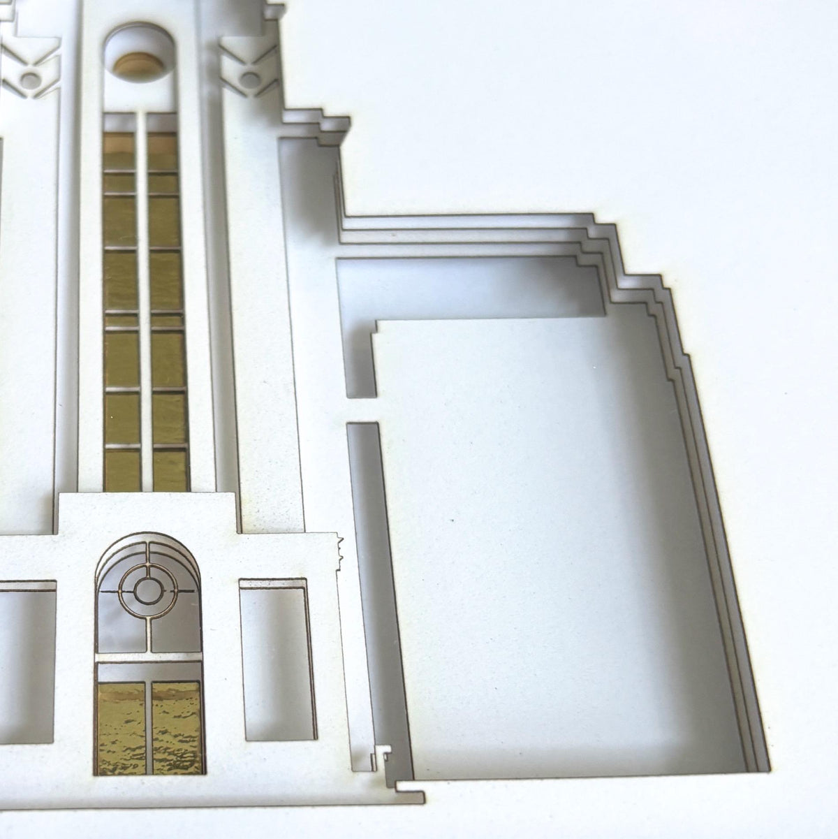 A close-up of a white laser-cut architectural model or model kit showing layered wood edges and cutout details against a white background. Boston Temple Art