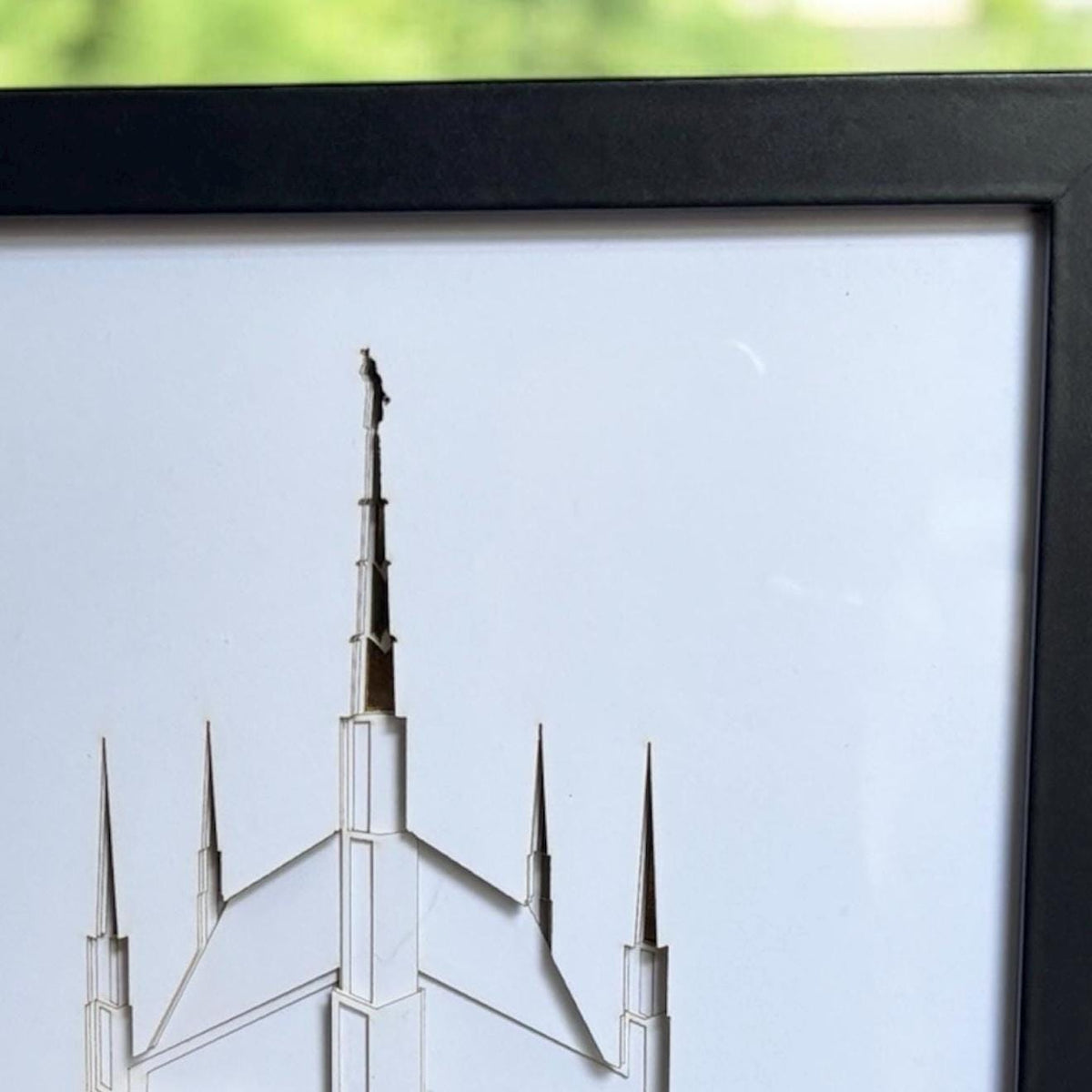 A close-up of a framed art print featuring a minimalist architectural illustration of a spired building, with a black frame and a light background.