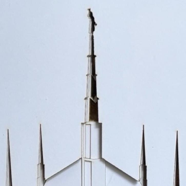 A close-up architectural view of a white spire with multiple pointed metal peaks against a pale blue sky. Dallas Temple Gift