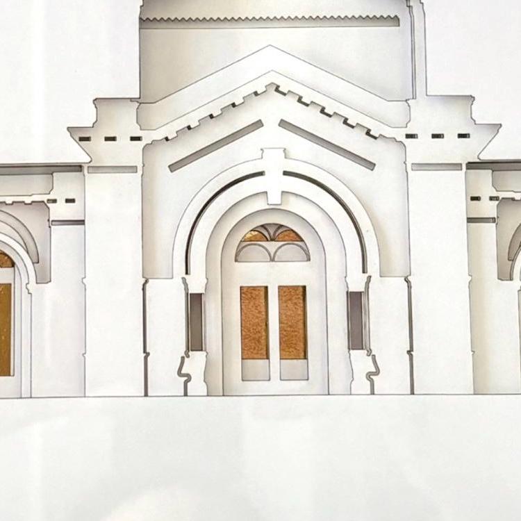 A close-up of a white architectural model or paper cutout showing a detailed arched doorway with decorative molding and small tan window panels. Fort Collins Temple Art