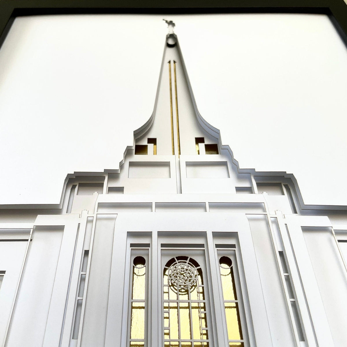 A low-angle view of a white temple-style building facade with a tall pointed spire, decorative trim, and tall windows with warm yellow-gold light visible inside.