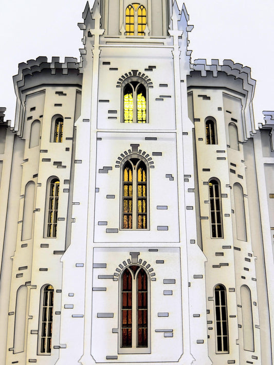 A close-up architectural view of a white castle-like building facade with arched windows, gray stone accents, and warm yellow light glowing from the windows against a pale sky.