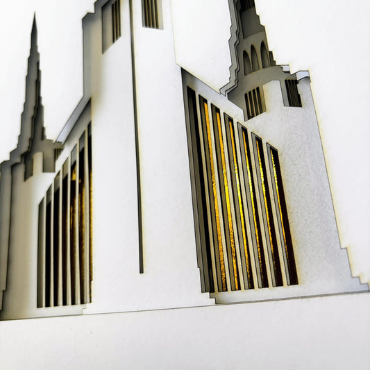 A laser-cut wooden architectural model of a cathedral, featuring white wood layers with cutouts and golden wood accents in the window-like sections, set against a plain white background.