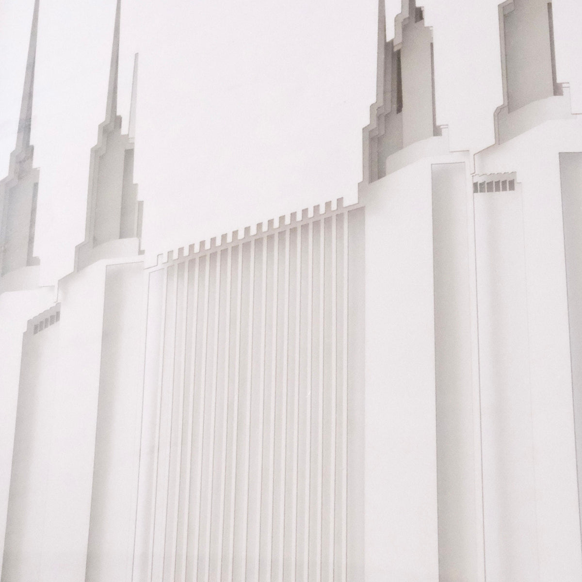 A close-up architectural photograph of a white temple-like building with tall spires and vertical ribbed detailing, shown against a very light neutral background.